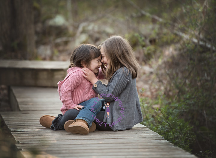 Two girls sitting and giggling and hugging outdoors. 